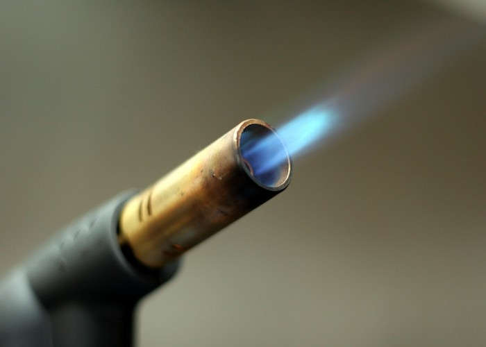 Close-up of a propane blowtorch tip with a blue flame shooting out.